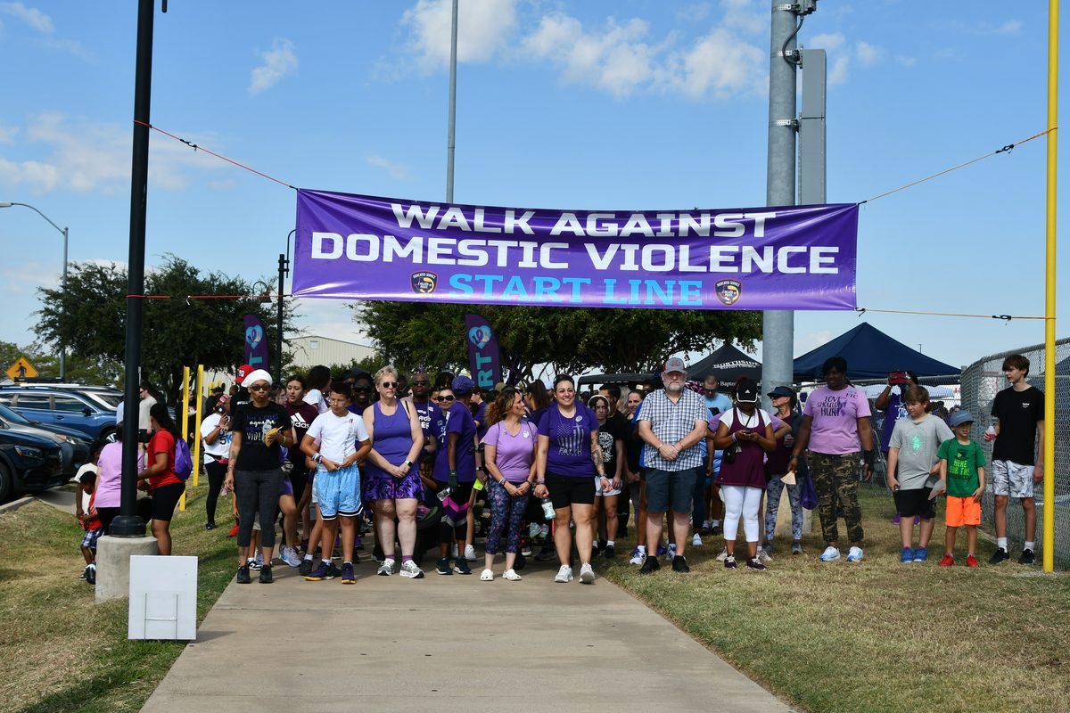 Community members gathered at the start line beneath the Walk Against Domestic Violence banner